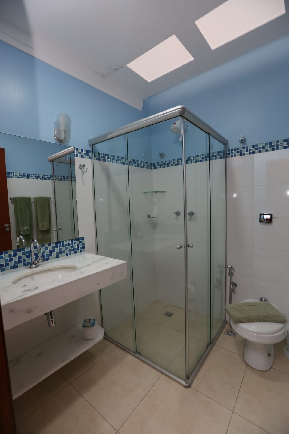 Banheiro com box de vidro e acabamento em mosaico